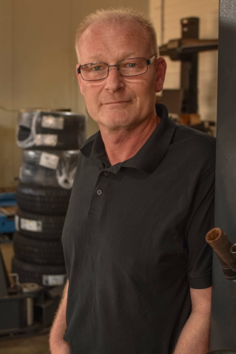 Guido Schnichels lehnt lächelnd an der Hebebühne in der Werkstatt.