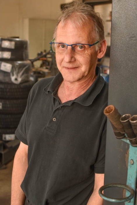 Guido Schnichels lehnt lächelnd an der Hebebühne in der Werkstatt.
