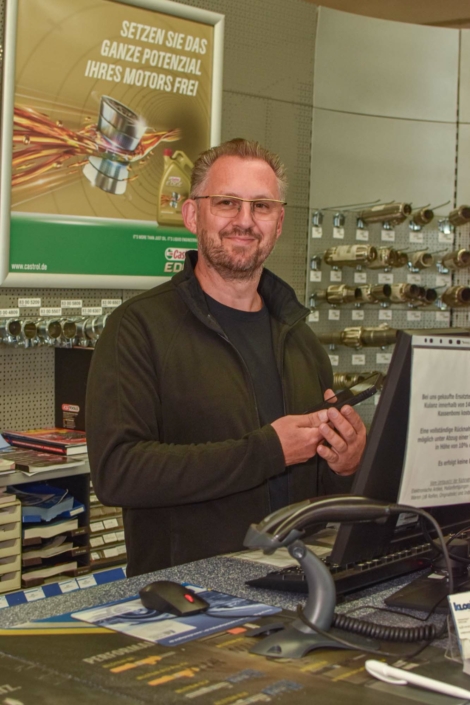 Heiko Schneider steht lächelnd an der Kasse des Autoteile-Shops in Kall.