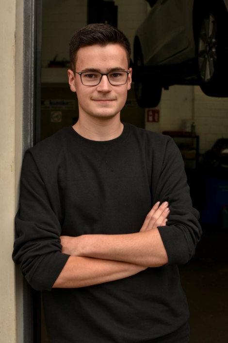 Louis Krogull lehnt mit verschränkten Armen, lächelnd an der Innenseite des Werkstatttores.
