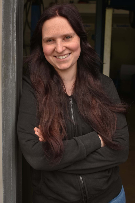 Melanie Lindemeier lehnt mit verschränkten Armen, lächelnd an der Innenseite des Werkstatttores.